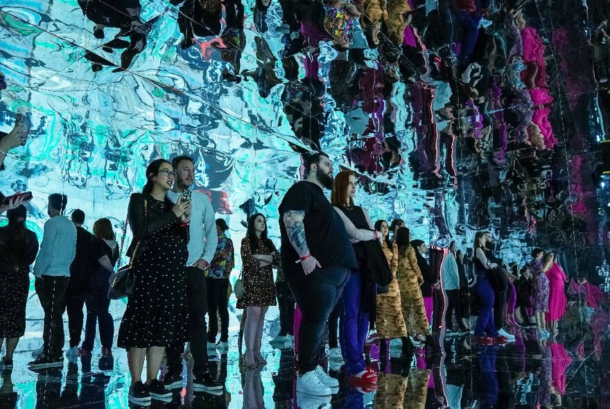 People standing in a mirrored room, surrounded by distorted reflections.