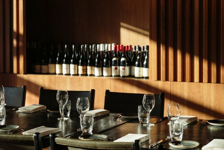 Vintage wines displayed on a timber shelf with a long dining table set for a wine-tasting dinner in front of it.