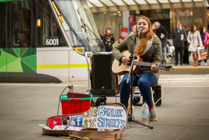 A busker performs in a busy street wth a tram going past in the background. 