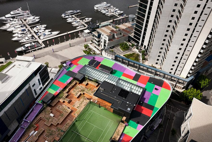 Sebel Docklands hotel viewed from the air with rooftop tennis court and seating areas, Docklands marina and towers in the background.
