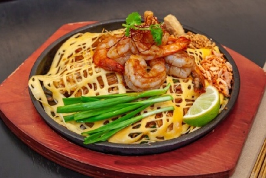 A Thai pancake dish topped with prawns, spring onions and lime, on a red tray.