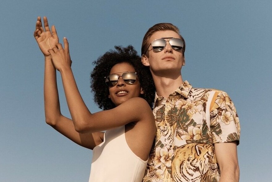 Male and female models wearing sunglasses looking into the sun against a blue sky.
