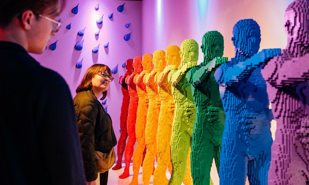 Two people looking at a display of rainbow coloured life-sized LEGO statues.
