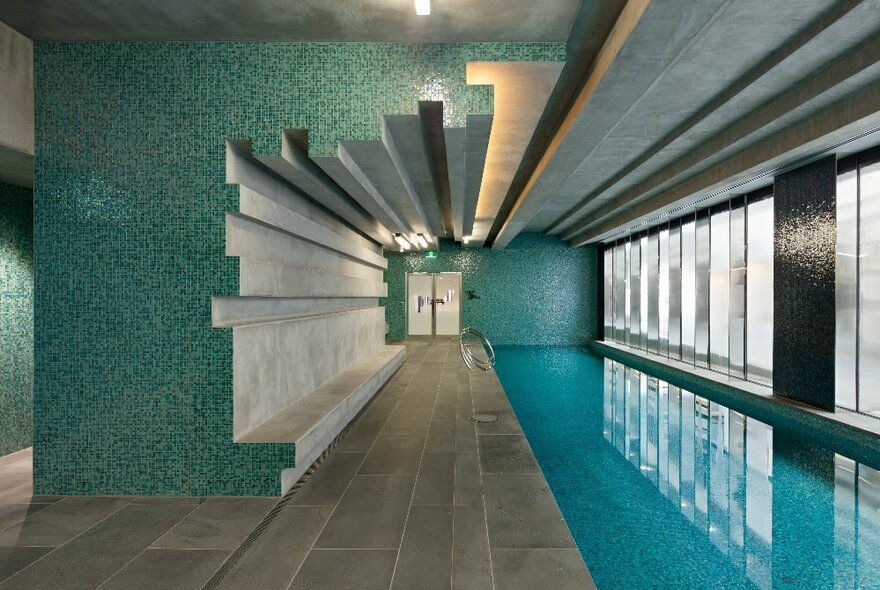 Blue-tiled indoor pool with long narrow lap lanes beneath long row of windows.