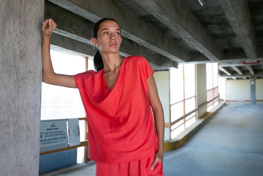 Female model wearing a loose red top with a cowl neckline and a matching coloured skirt, posed in an empty underground car park.
