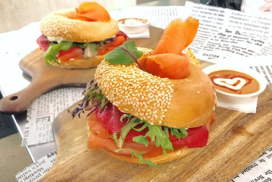 Two sesame seed bagels filled with smoked salmon and lettuce, on wooden serving boards.