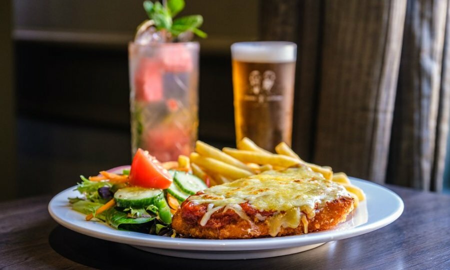 A chicken parma on a plate in front of a cocktail