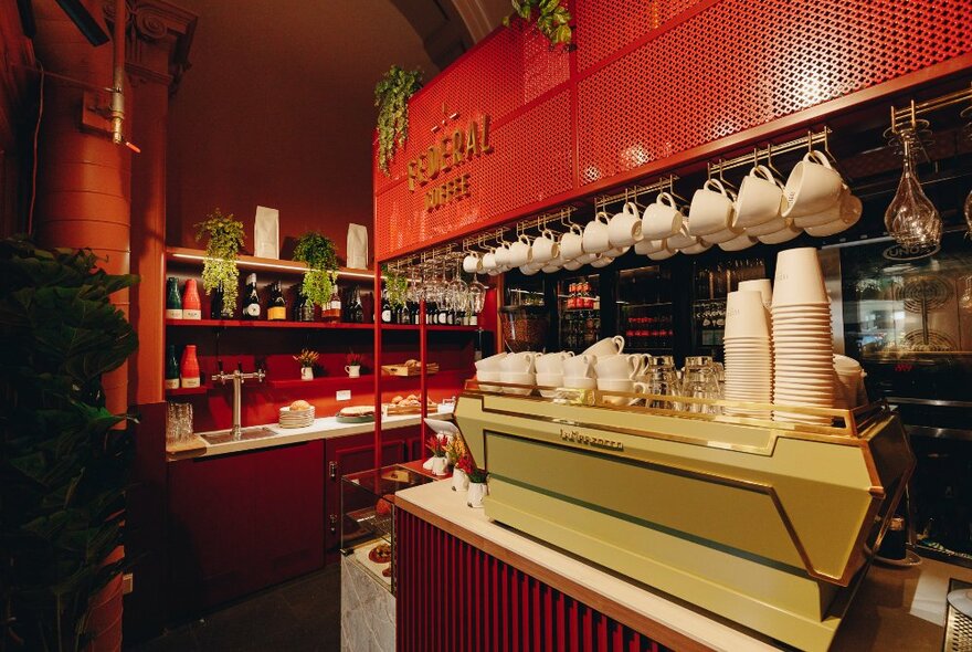 A red-themed coffee shop interior with La Mazarcco coffee machine and hanging mugs.