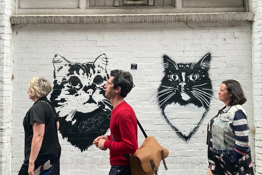 People walking past cat graffiti in a Melbourne laneway.