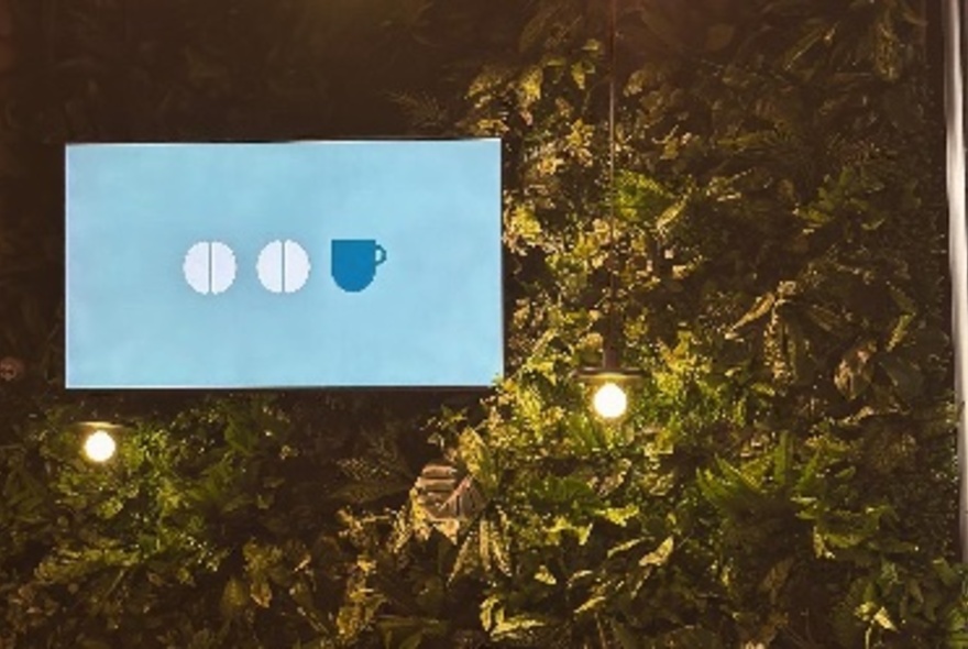 Pale blue signage against trees, with small lights below.