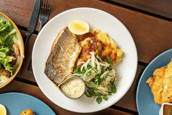 Dish of grilled fish with potato gratin and salad, served with lemon wedges.