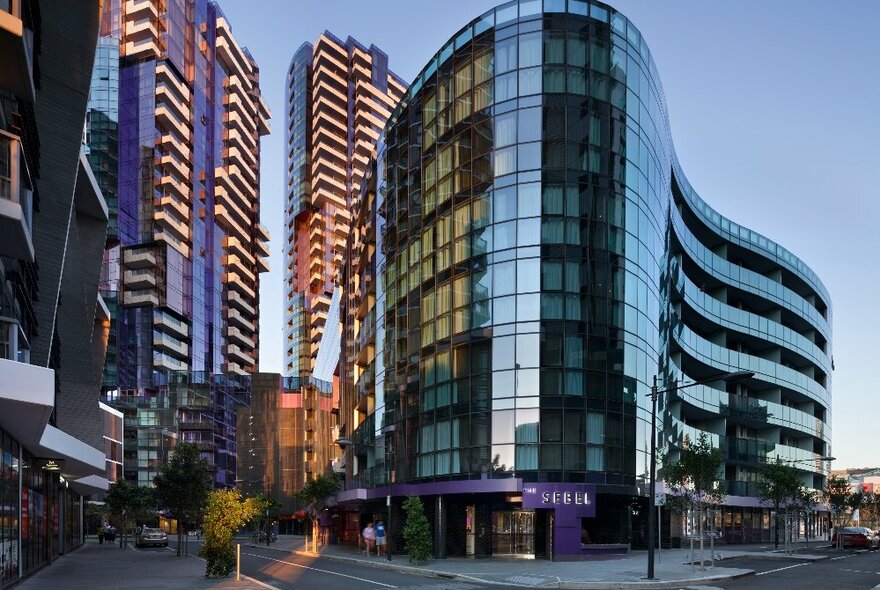Curved glass exterior of Sebel Hotel Docklands, with other city buildings in the background.