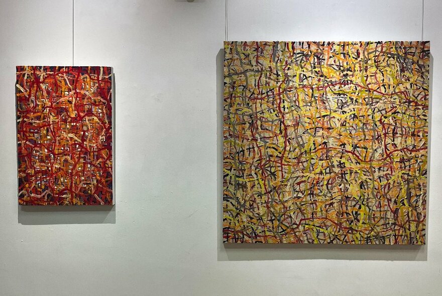 Two abstract paintings on canvas, composed of many squiggly intersecting and overlapping lines, hanging on a white wall in a gallery space.