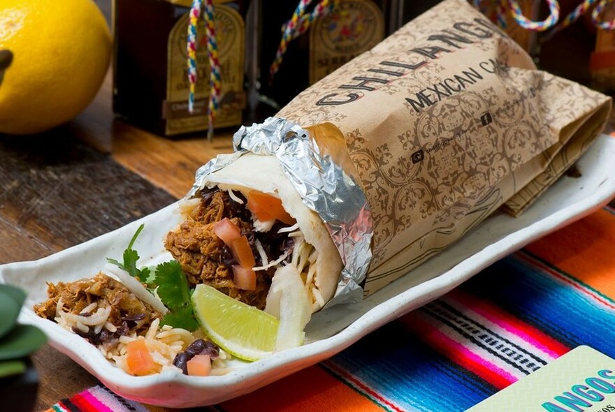 A wrapped burrito on a plate and a colourful tablecloth on the table. 